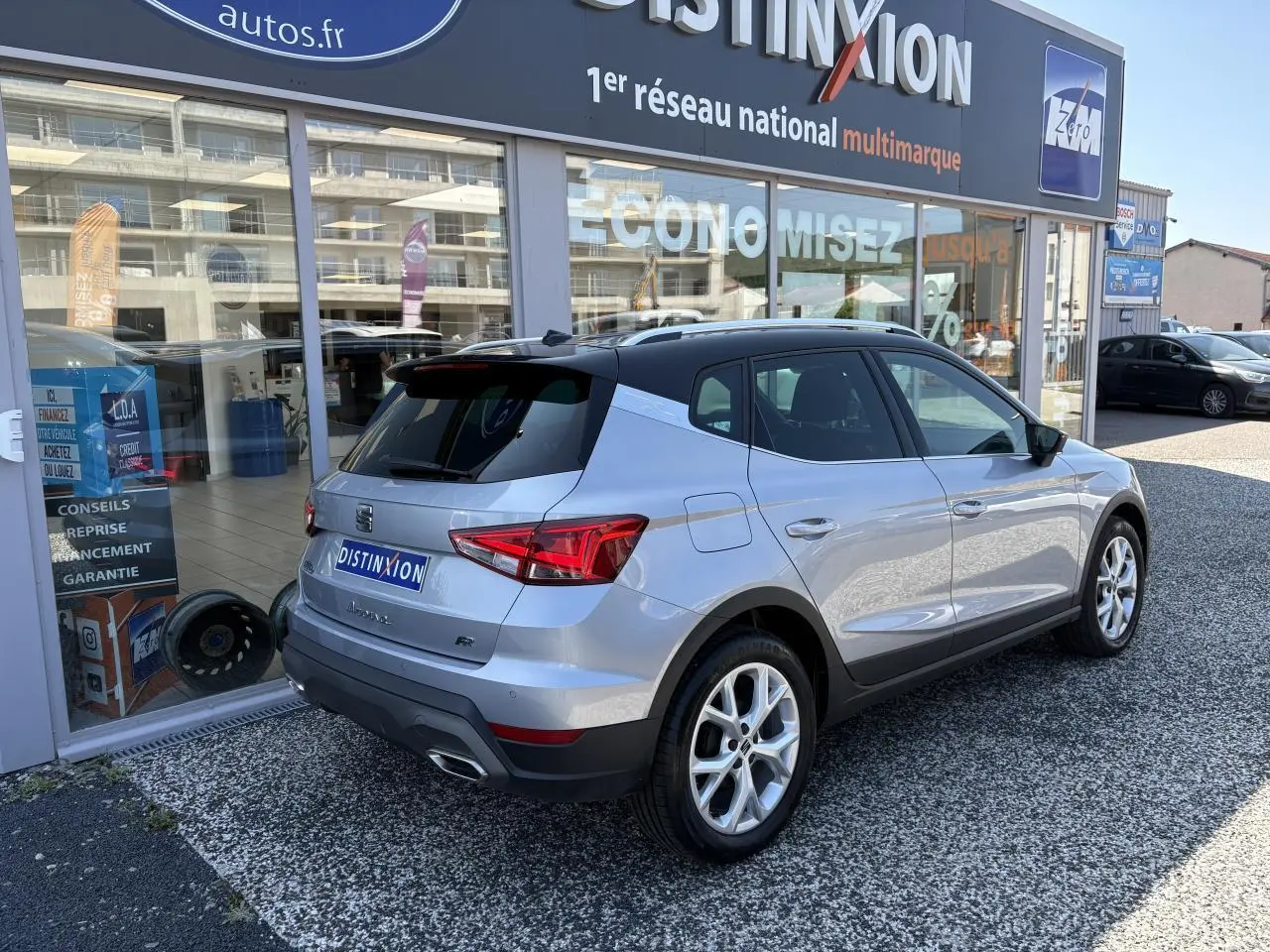 Vue 3/4 arrière droite d'un SEAT Arona 2024 gris GRS avec jantes alliage et logo FR devant un showroom.