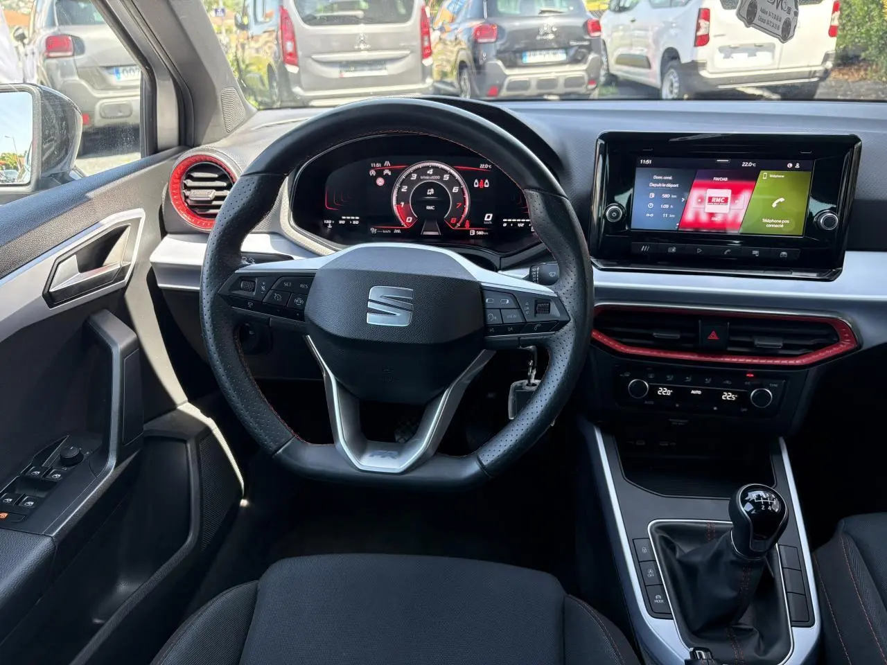 Intérieur de la SEAT Arona 2024 vu du siège conducteur, volant sport cuir, détails rouges autour des aérateurs et console centrale.