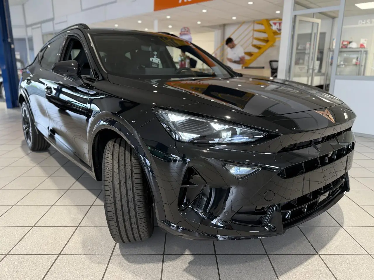 Vue 3/4 avant d'une CUPRA Formentor 2025 noir Night avec logo cuivré et jantes alliage 18'' en showroom.