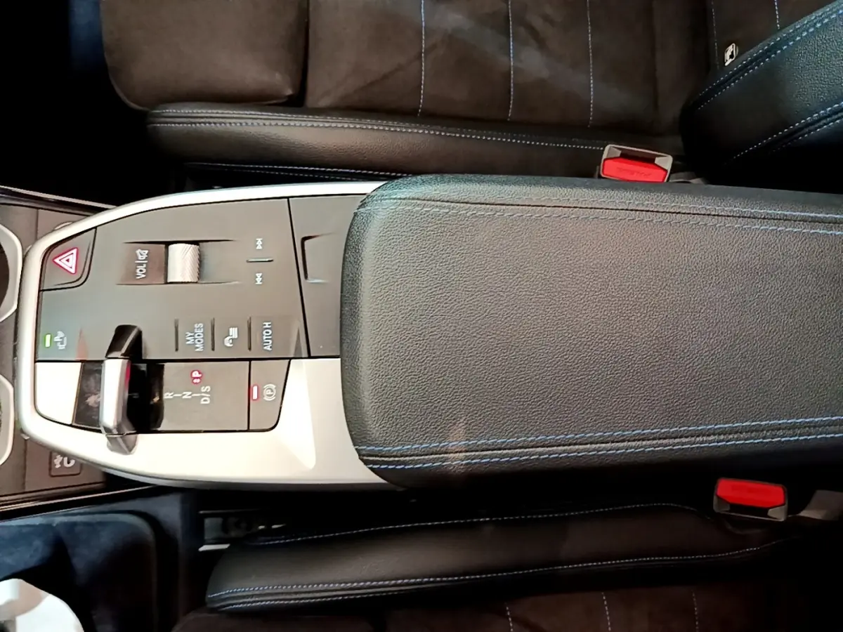 Vue plongeante sur la console centrale noire du BMW X1 xDrive23i M Sport 2023 avec accoudoir et commandes tactiles.