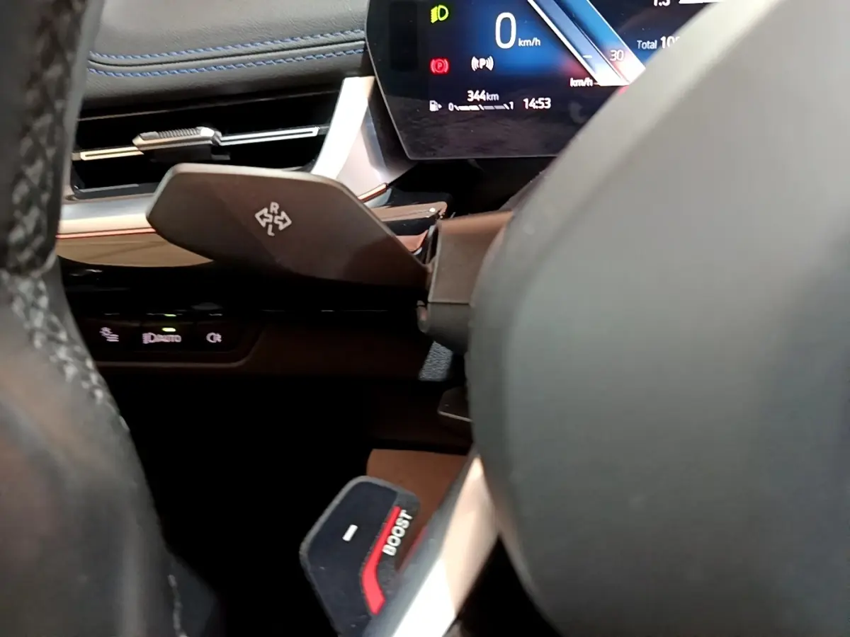 Gros plan sur le volant noir et le levier de commande derrière, avec l'affichage digital du tableau de bord d'une BMW X1 xDrive23i M Sport.