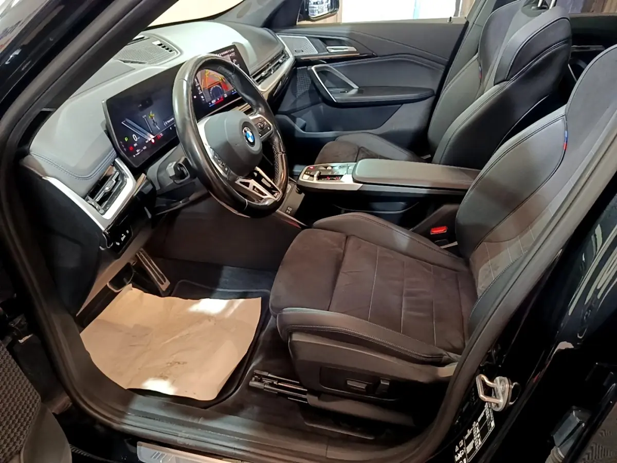 Vue intérieure côté conducteur du BMW X1 xDrive23i M Sport 2023 noir, avec sièges sport et tableau de bord digital.