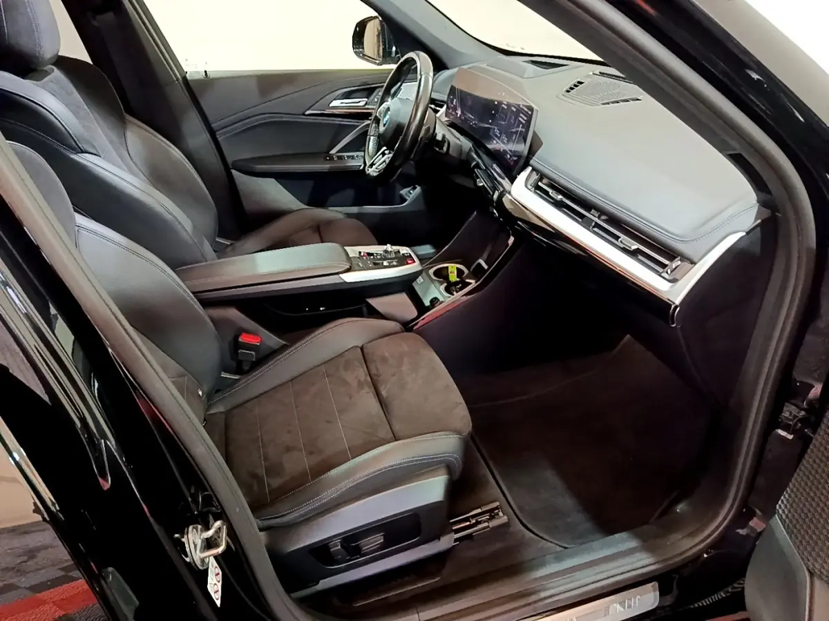 Vue intérieure côté conducteur du BMW X1 xDrive23i M Sport 2023 noir, avec sièges en cuir et tableau de bord digital.
