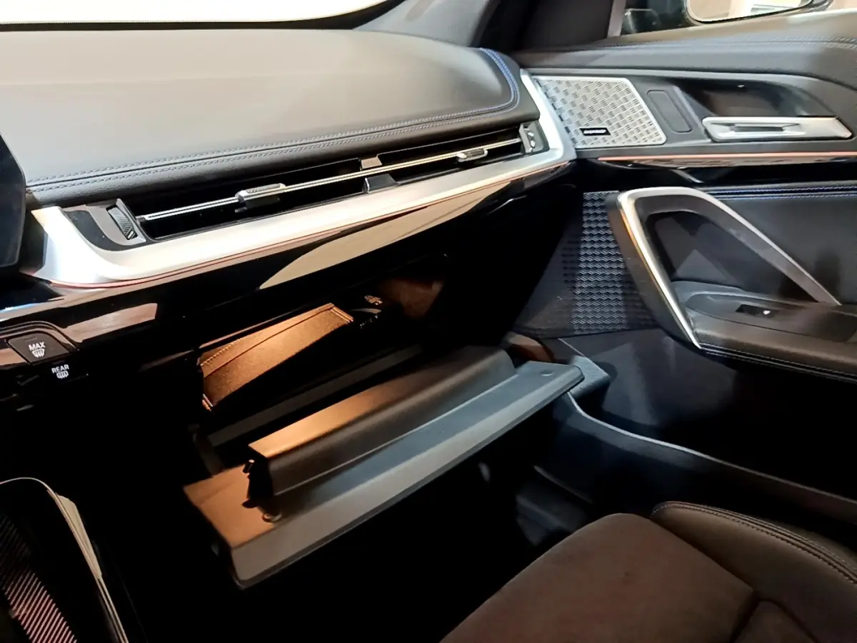 Intérieur BMW X1 xDrive23i M Sport 2023, vue côté passager sur boîte à gants ouverte et tableau de bord noir.