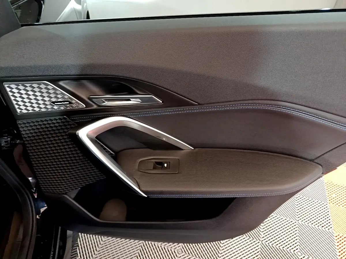 Vue intérieure du panneau de porte côté gauche du BMW X1 xDrive23i M Sport 2023 avec surpiqûres bleues et insert carbone.