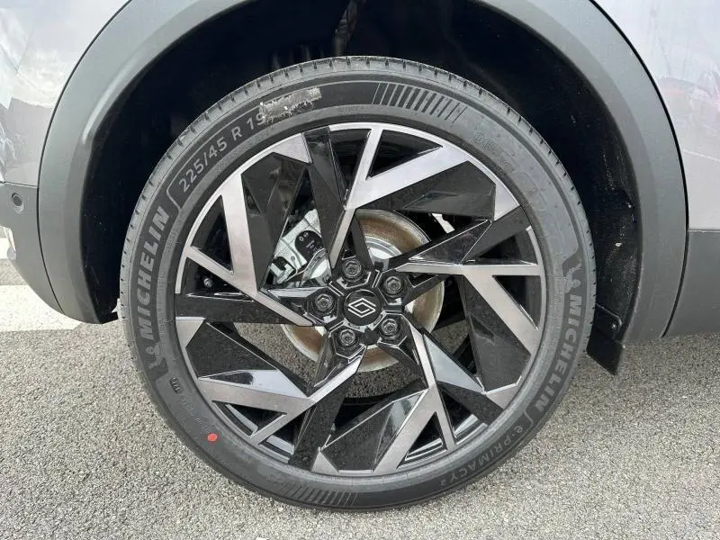 Gros plan sur la roue avant droite du Renault Captur 2026 gris Cassiopée/Noir Étoilé avec jante noire et grise au design géométrique.