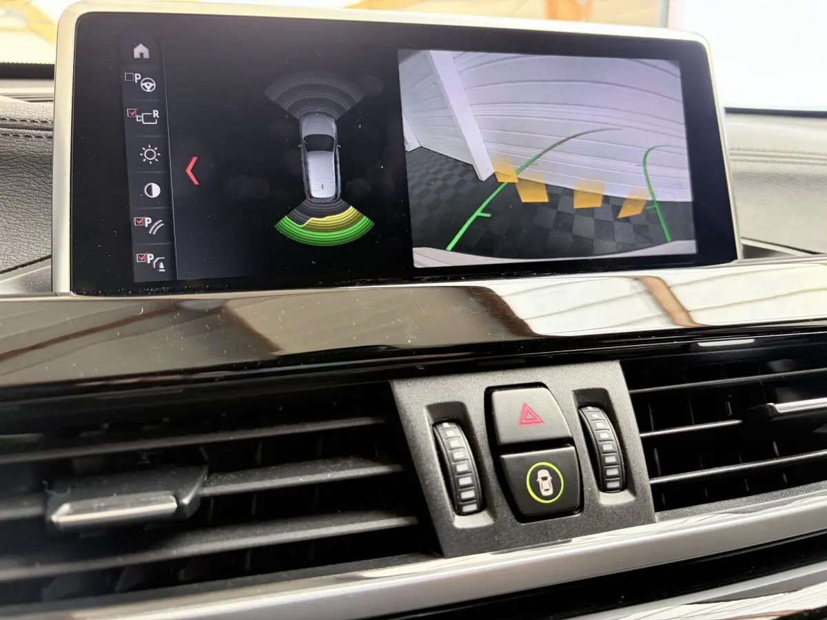 Vue rapprochée de l’écran tactile du tableau de bord du BMW X1 blanc, affichant l’aide au stationnement arrière.