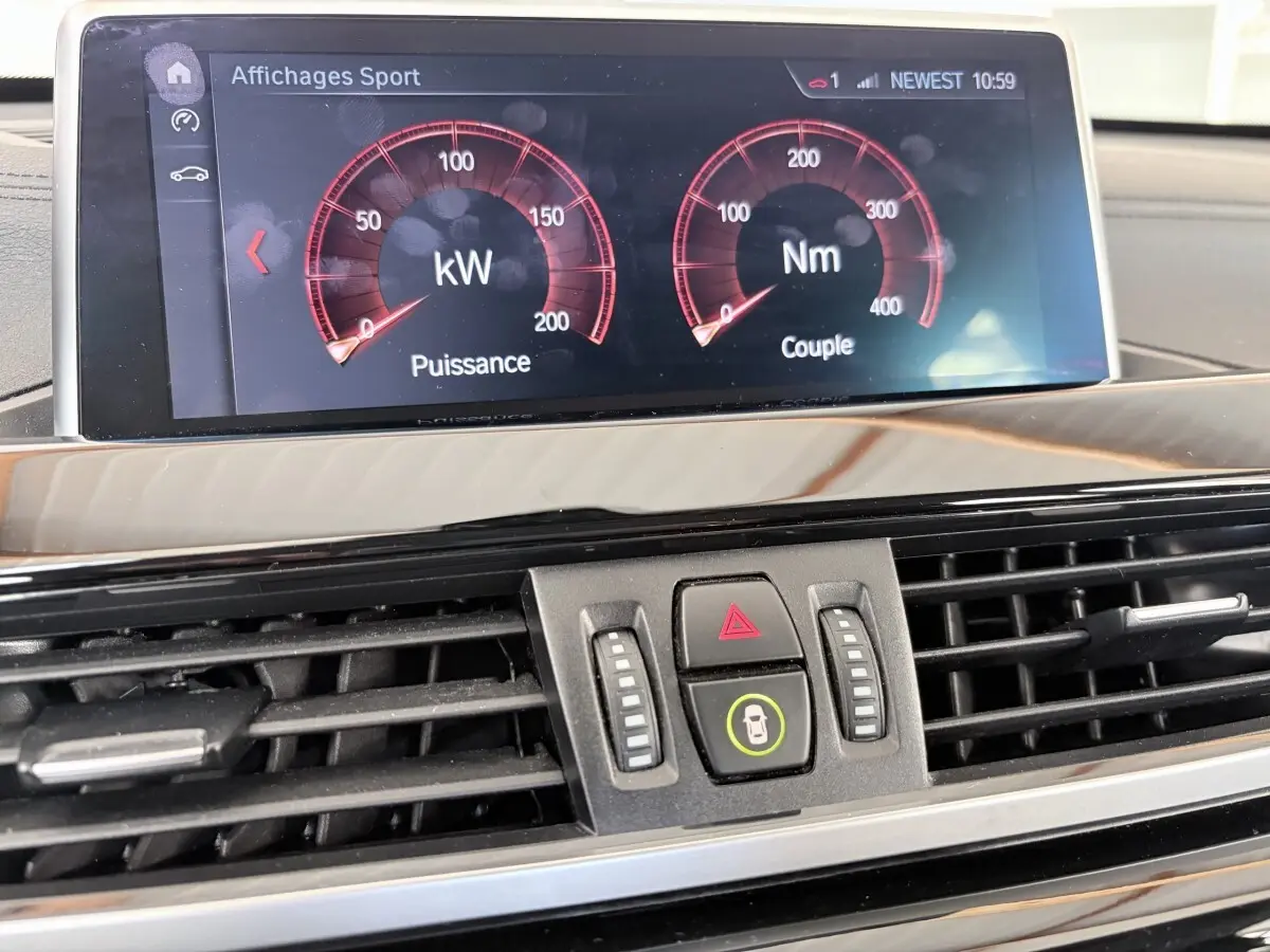 Gros plan sur l'écran tactile et la console centrale noire du tableau de bord du BMW X1 blanc, affichant les données de puissance et couple.