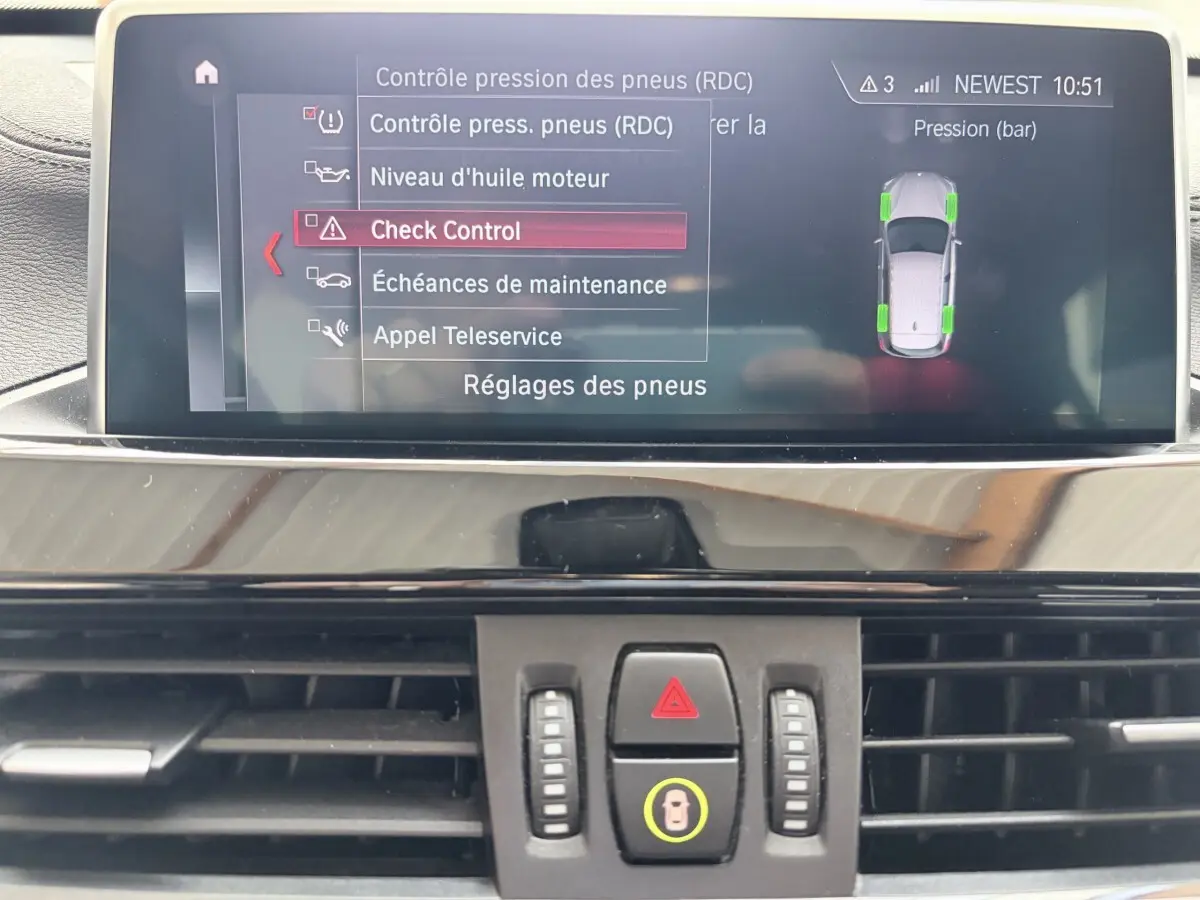 Écran tactile central du tableau de bord du BMW X1 blanc, affichant le menu de contrôle pression des pneus.