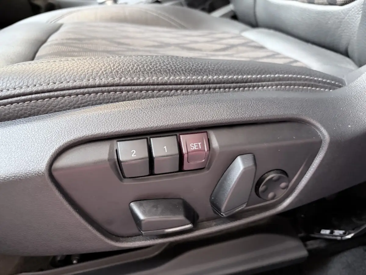 Détail des commandes de réglage électrique des sièges en cuir noir à gauche dans l’habitacle du BMW X1 blanc.