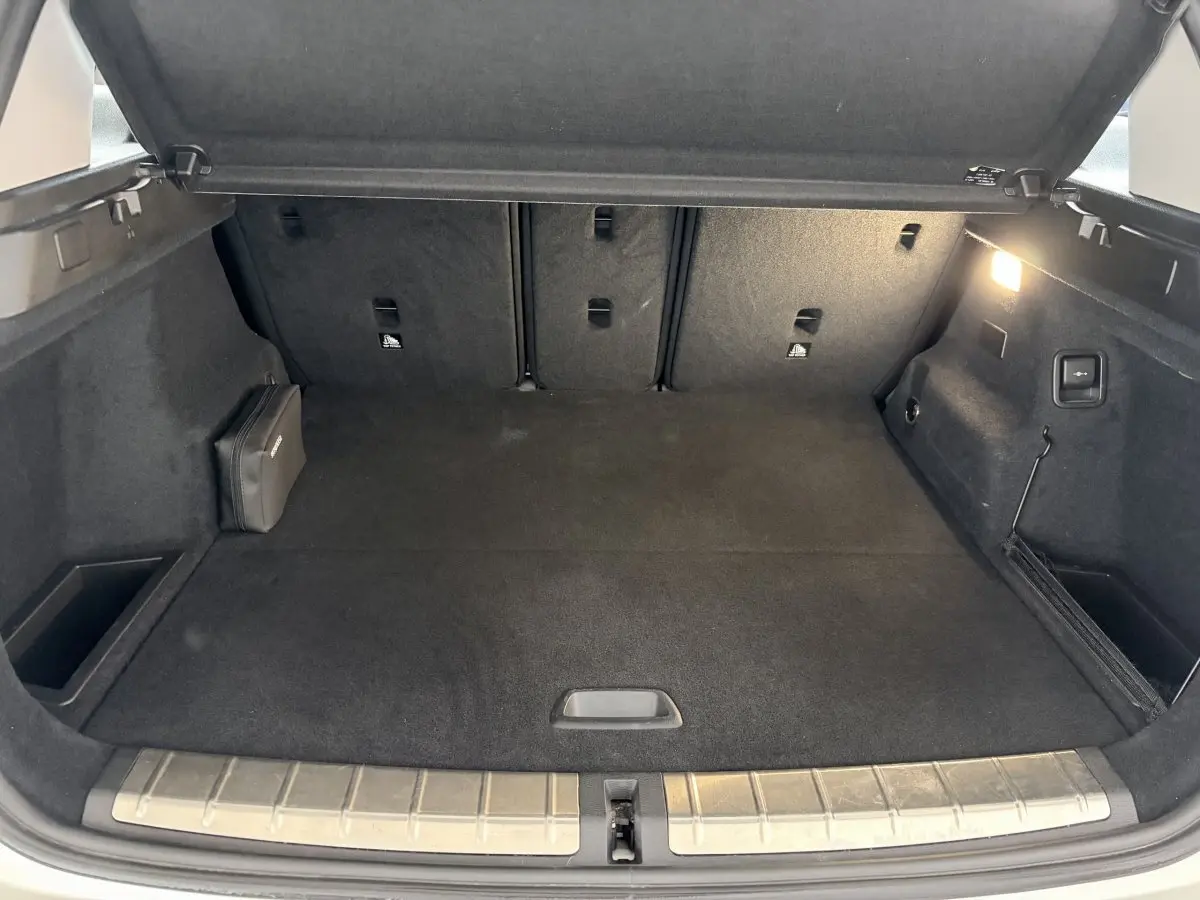 Coffre ouvert du BMW X1 blanc, vue intérieure arrière montrant un espace de chargement propre avec tapis noir et éclairage latéral.