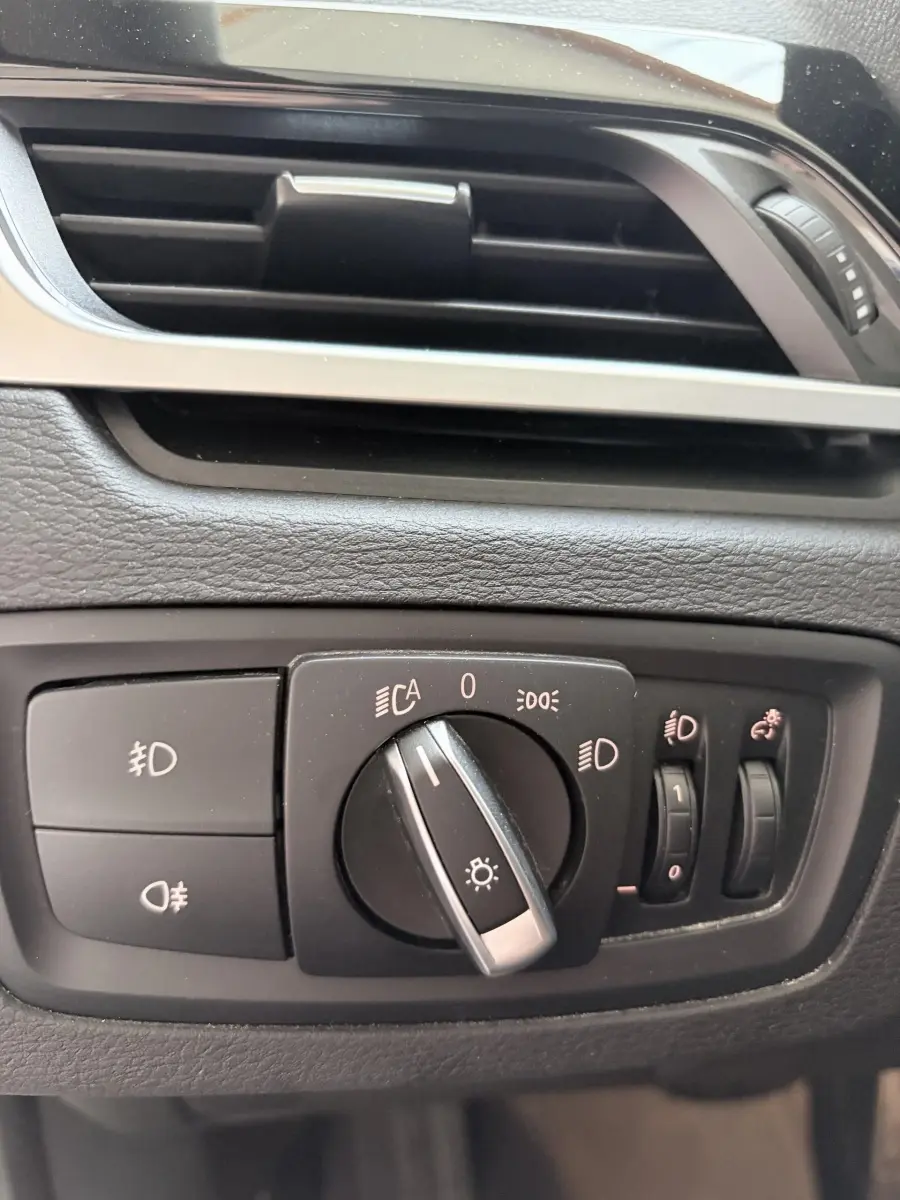 Gros plan sur les commandes d’éclairage et la sortie d’air du tableau de bord intérieur d’une BMW X1 blanche.