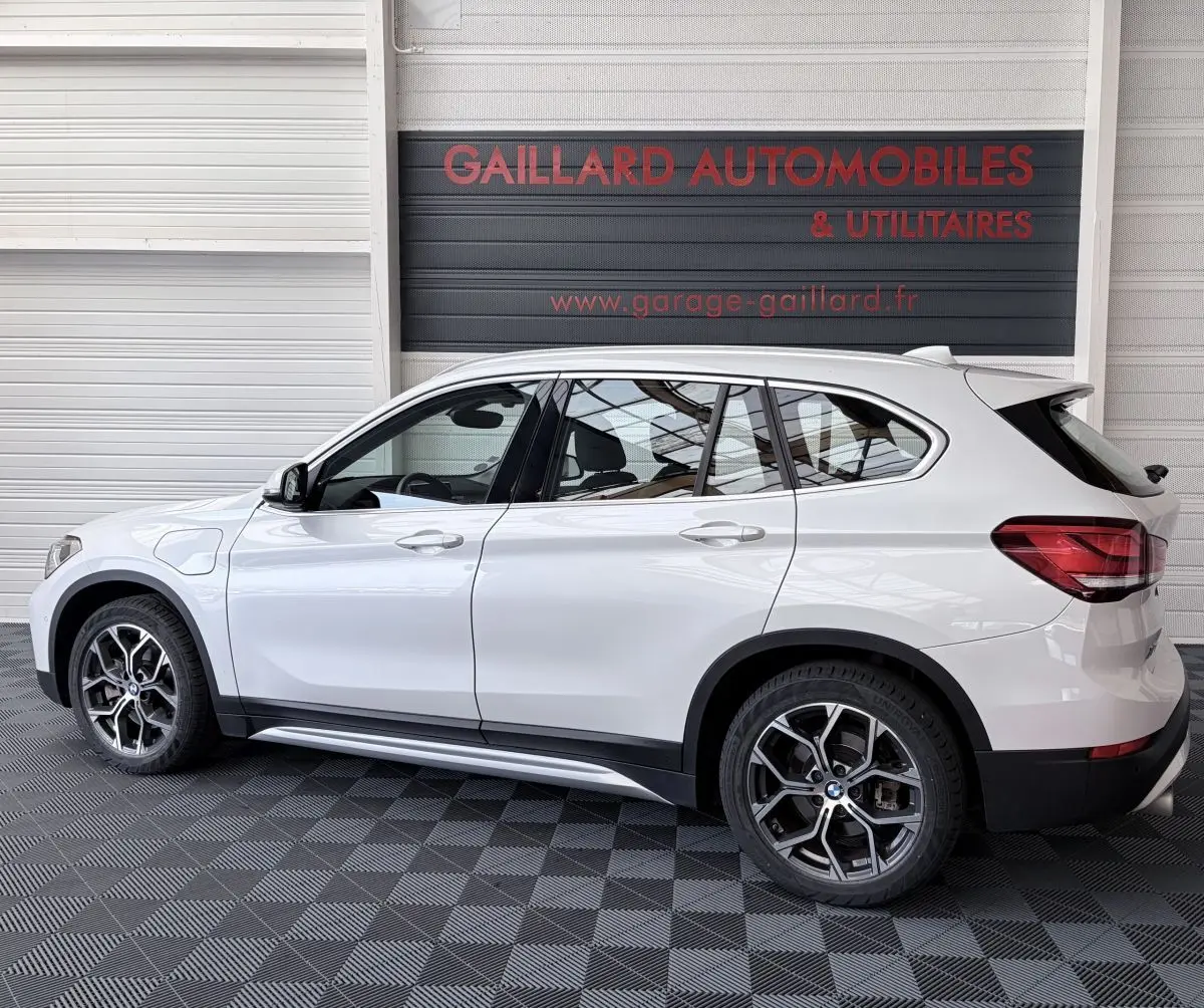 Vue latérale droite d’un BMW X1 blanc hybride rechargeable avec jantes alliage et rails de toit chromés.