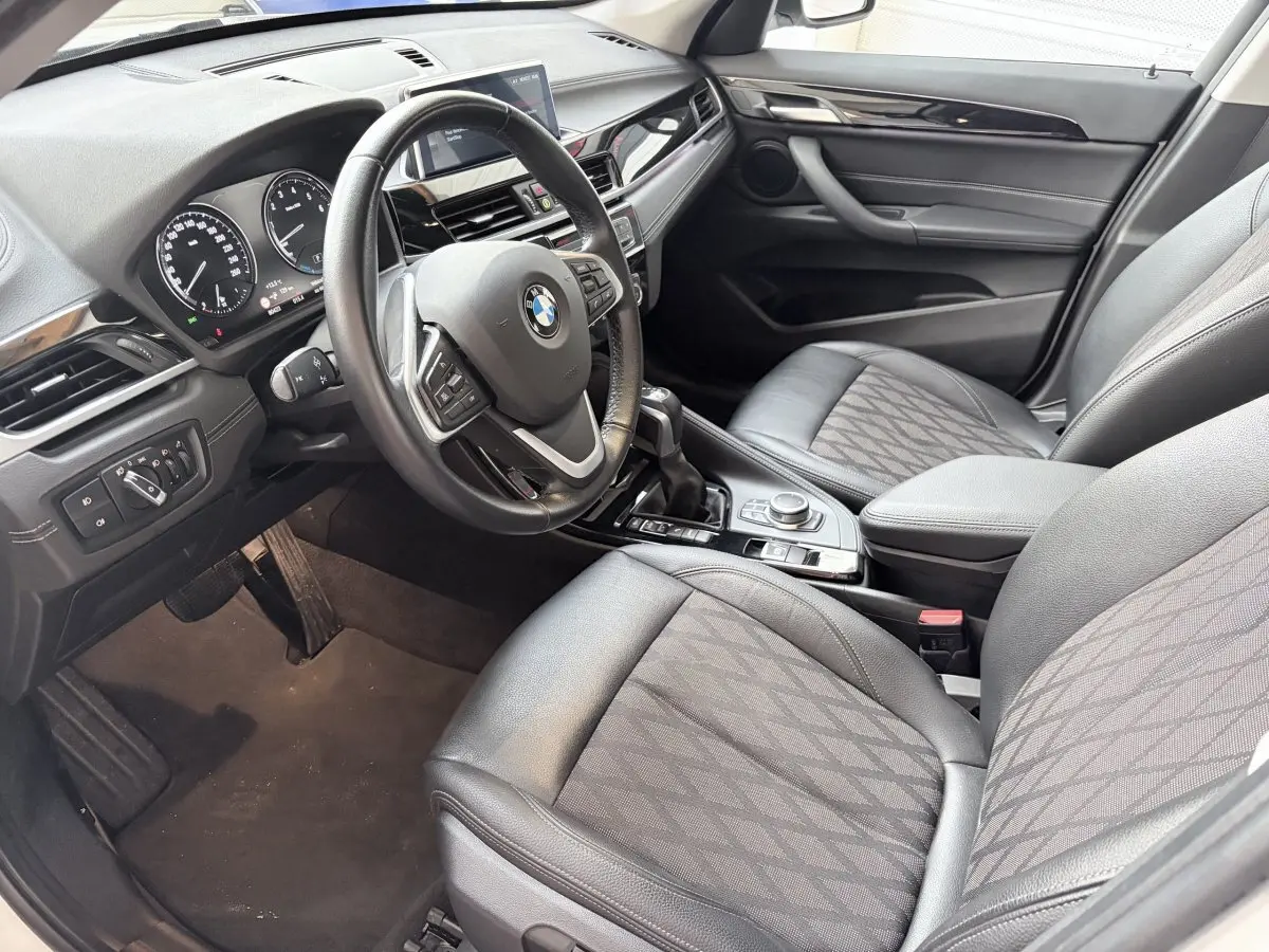 Vue intérieure côté conducteur d'une BMW X1 xDrive25eA xLine 2021 avec volant cuir alu multifonctions et sièges tissu noirs.