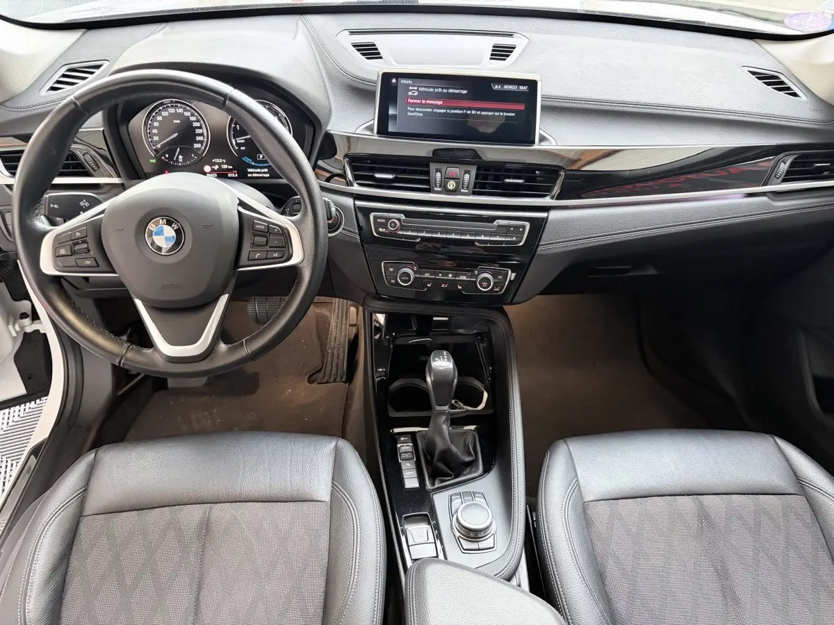 Vue intérieure avant de la BMW X1 xDrive25eA xLine 2021, volant cuir alu multifonctions et console centrale noire brillante.