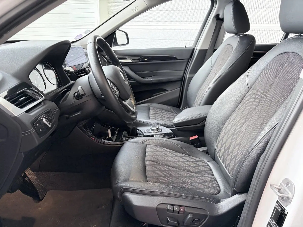 Vue intérieure côté conducteur de la BMW X1 blanche, montrant sièges en cuir et tissu avec motifs géométriques.