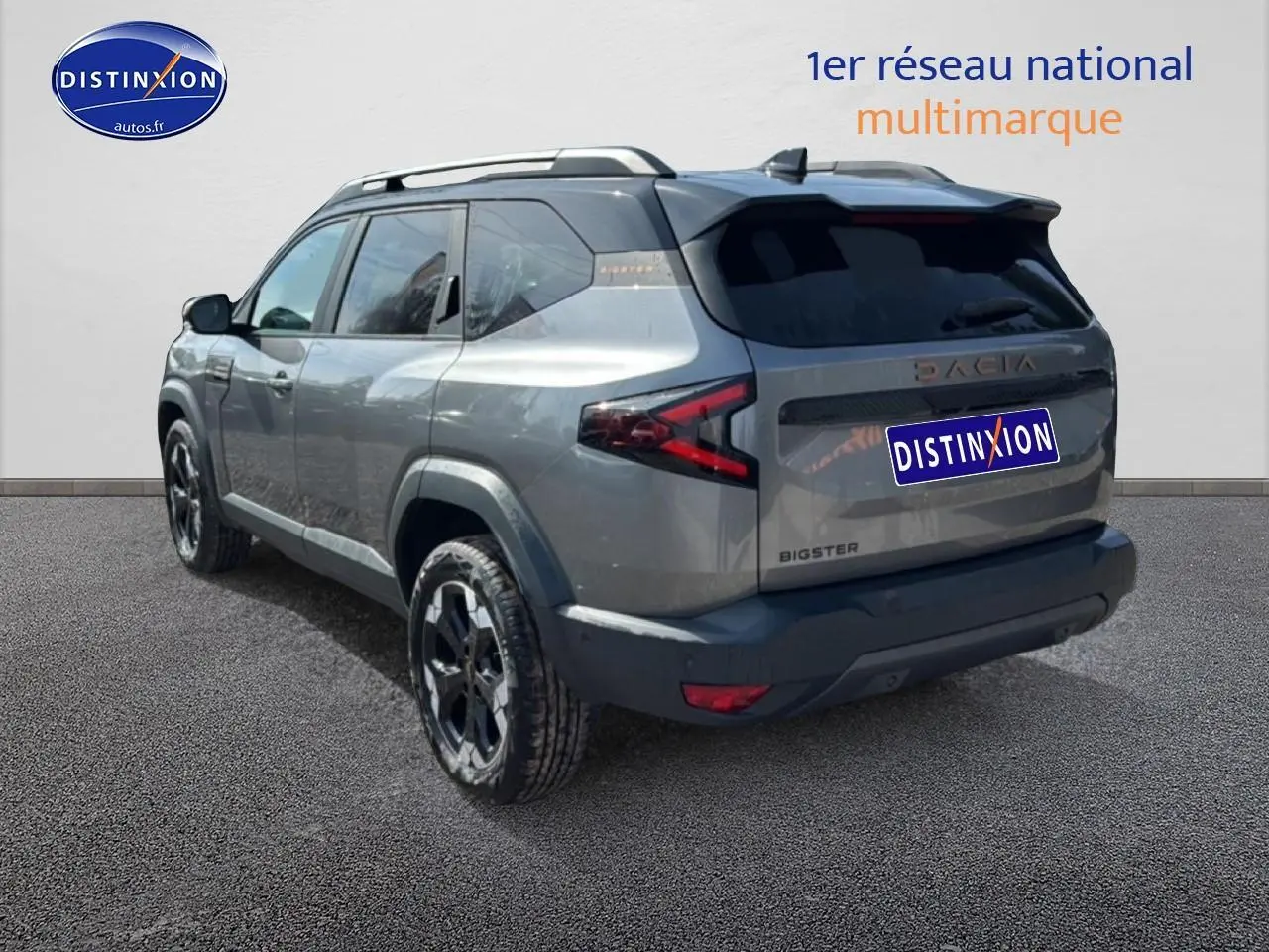 Vue 3/4 arrière droit d'un Dacia Bigster gris schiste avec jantes alu noires et barres de toit visibles.