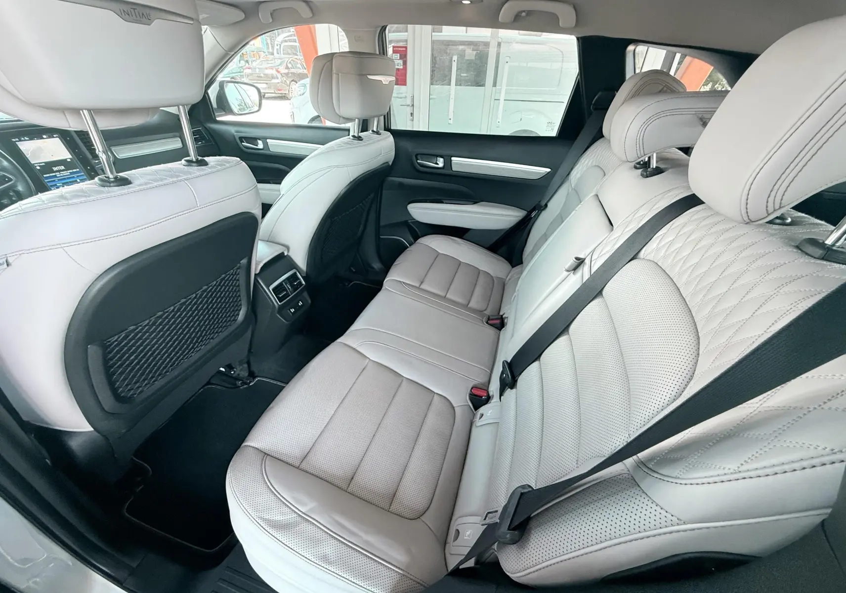 Vue intérieure arrière du Renault Koleos blanc 2021, sièges cuir beige clair avec surpiqûres et ceintures noires.