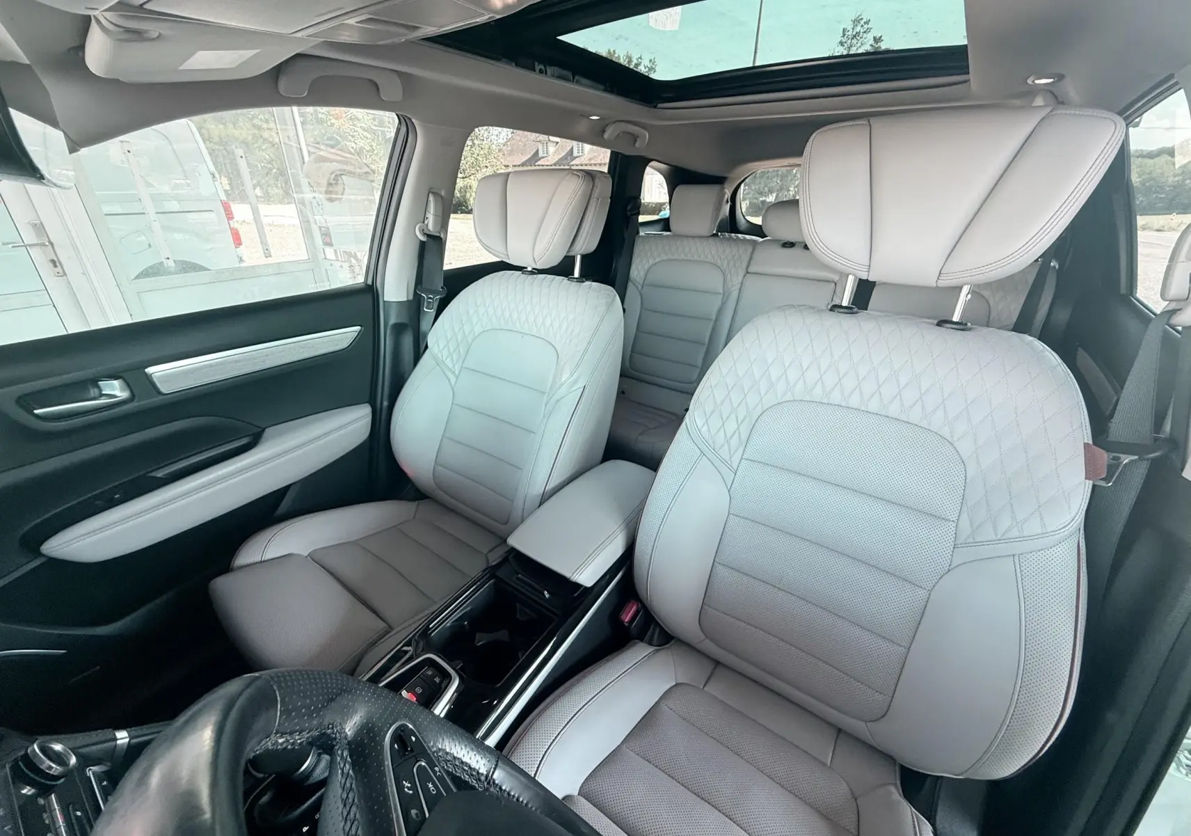Vue intérieure avant du Renault Koleos 2021 avec sièges cuir beige et toit panoramique lumineux.