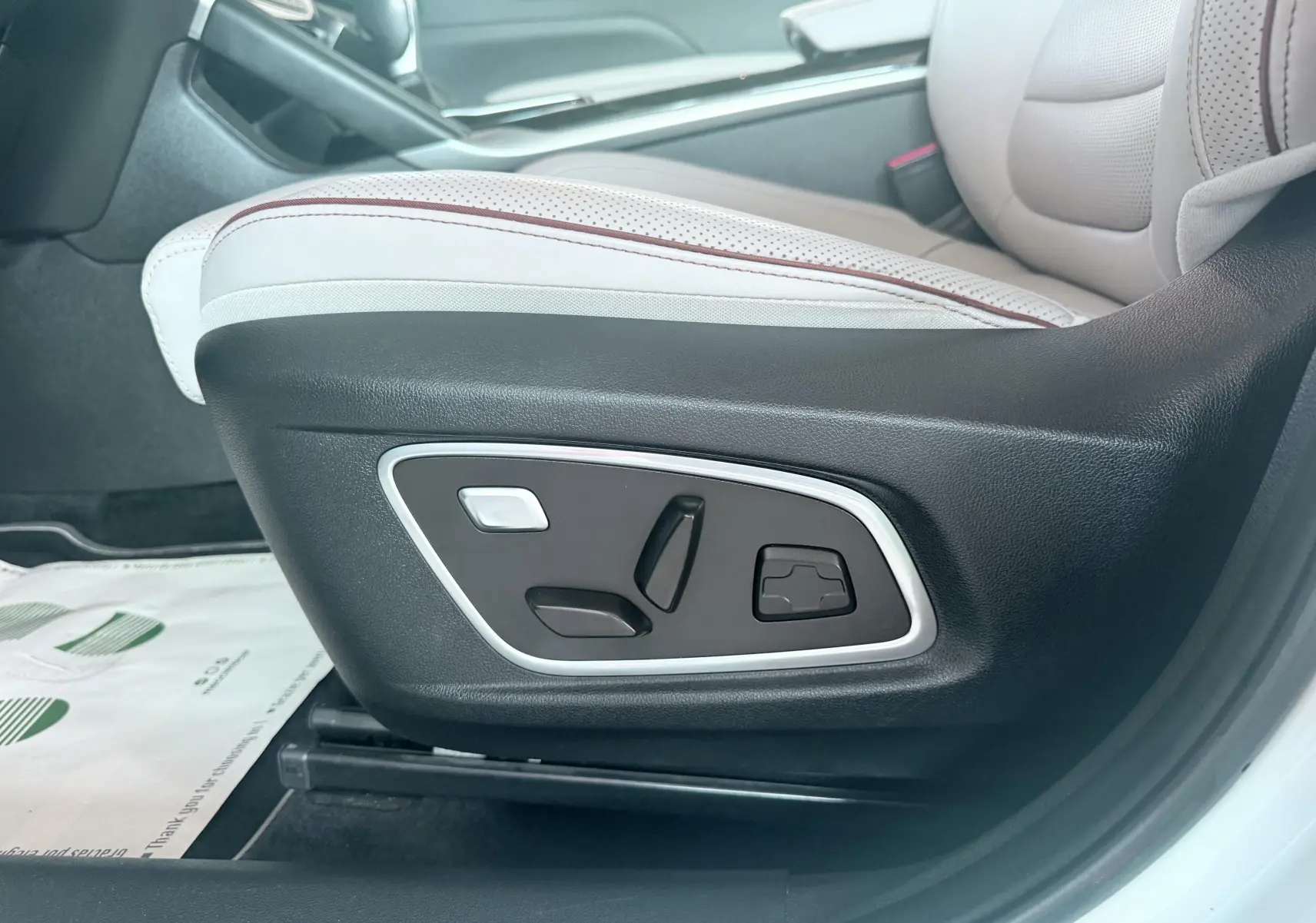 Gros plan sur les commandes électriques du siège avant droit en cuir beige et noir du Renault Koleos blanc 2021.