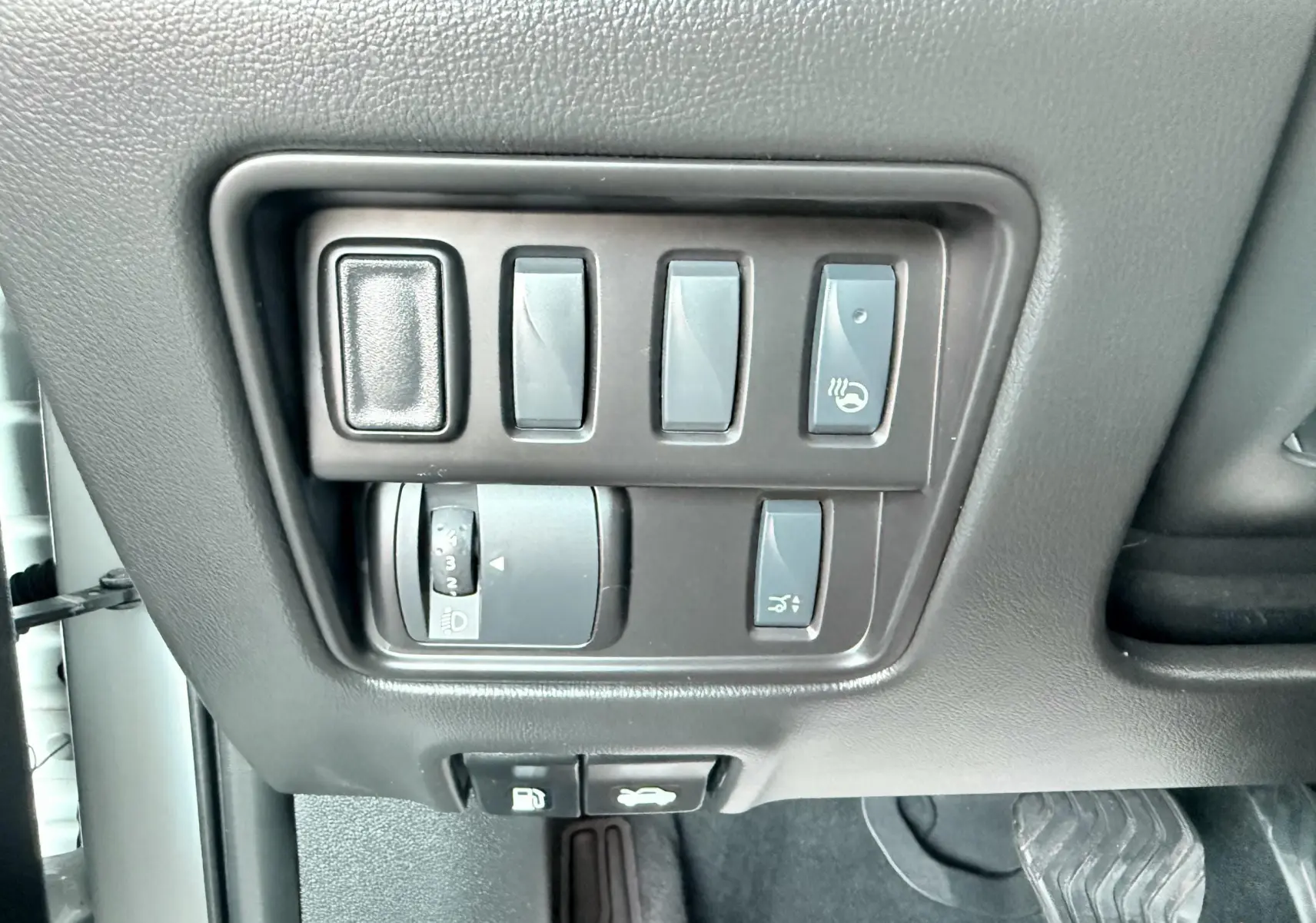 Gros plan sur les commandes de réglage des phares et du volant chauffant dans un Renault Koleos blanc, intérieur noir.