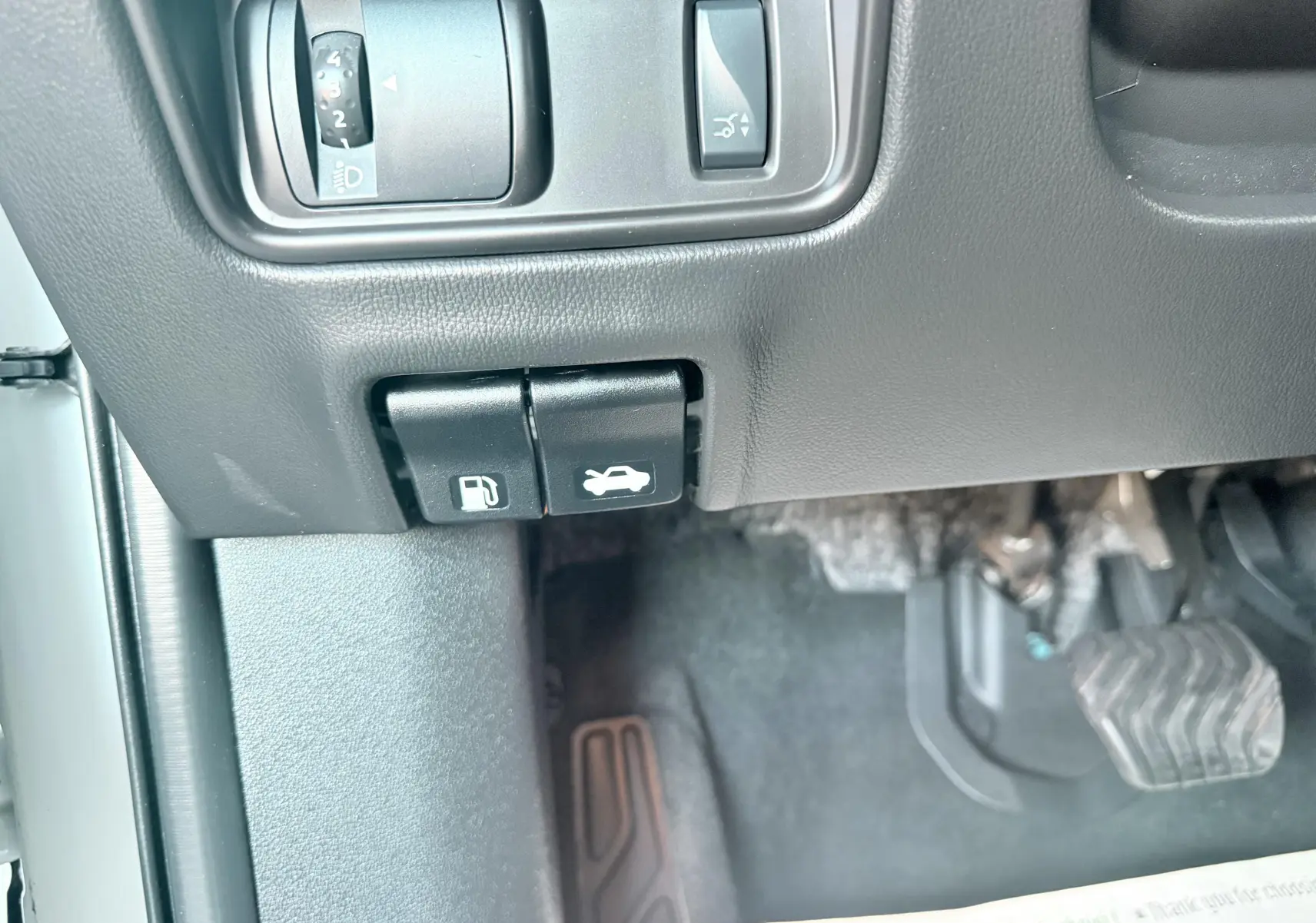 Gros plan sur les commandes d'ouverture du capot et de la trappe à carburant côté gauche d'un Renault Koleos blanc, 2021.
