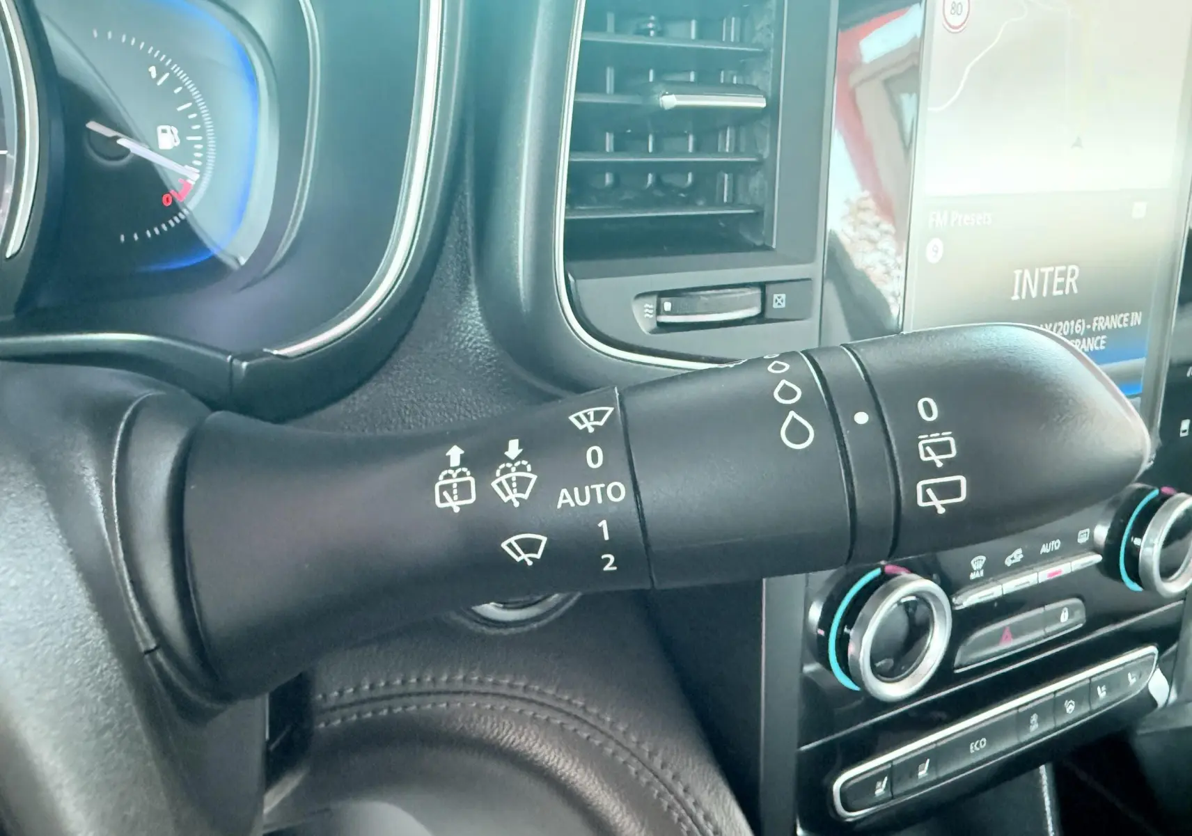 Gros plan sur la commande d’essuie-glace noire dans l’habitacle du Renault Koleos blanc, avec tableau de bord et écran tactile visibles.