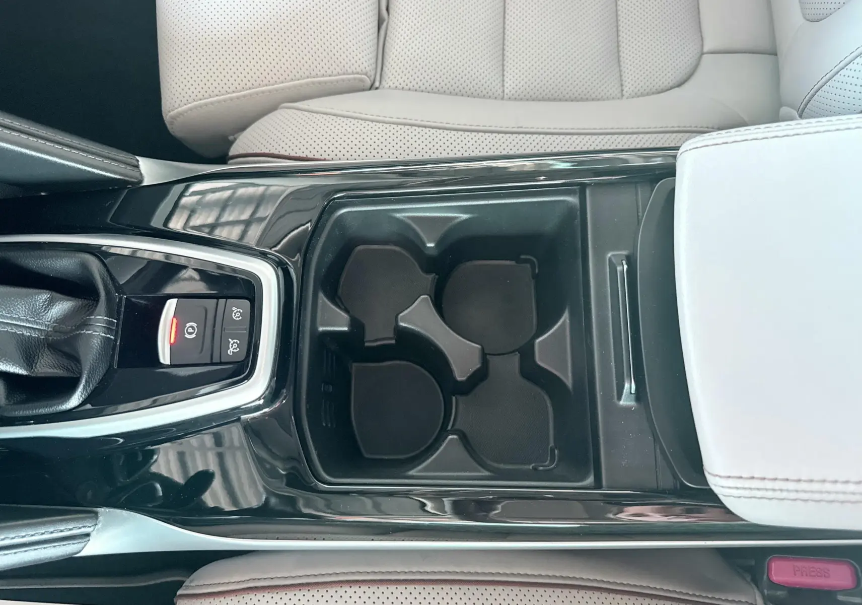Vue plongeante sur la console centrale noire avec porte-gobelets et accoudoir beige perforé du Renault Koleos blanc.