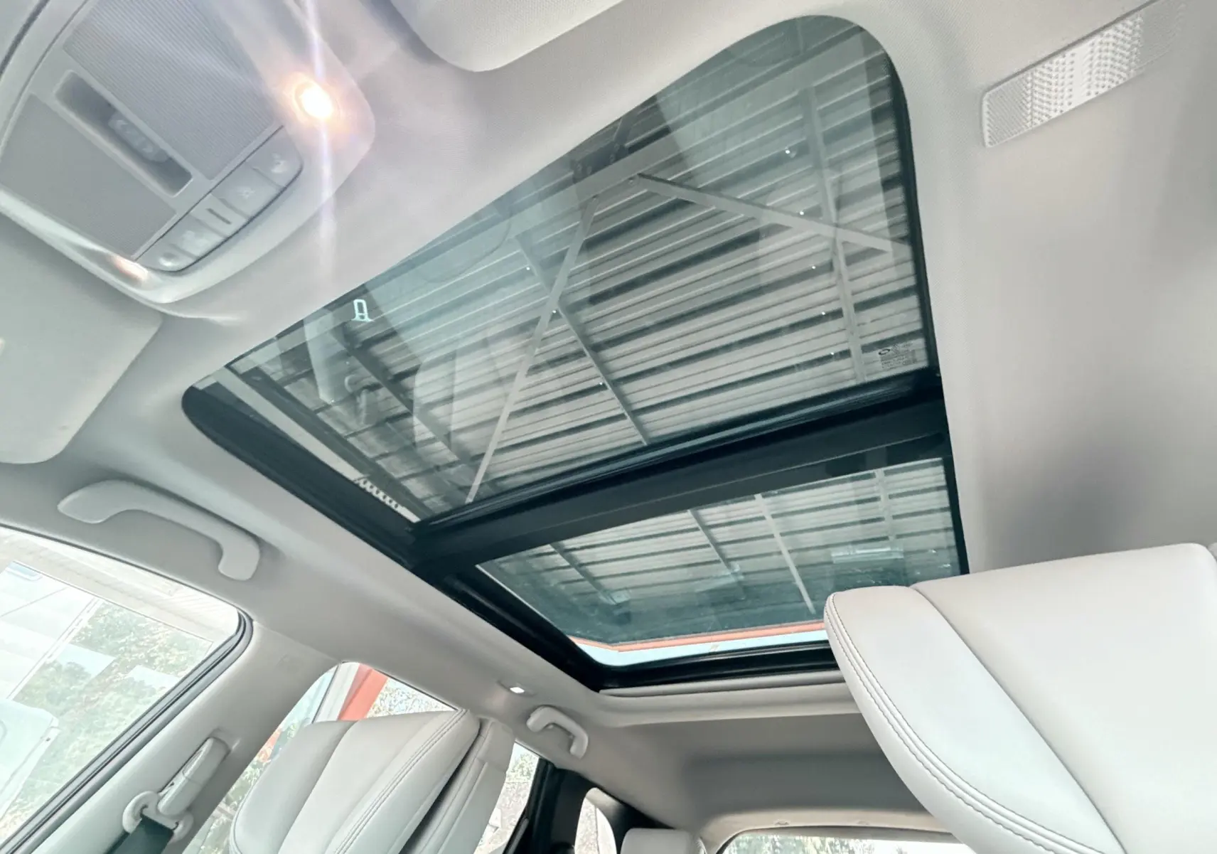 Toit panoramique en verre vu de l'intérieur avant du Renault Koleos blanc, avec sièges avant clairs visibles.