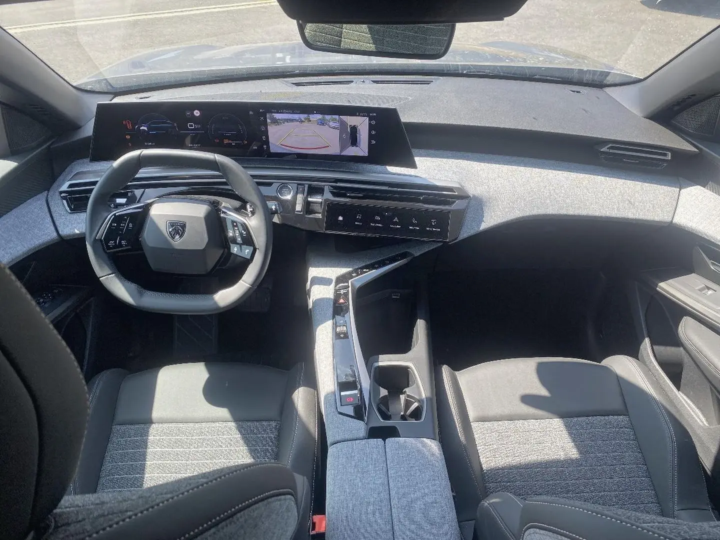 Vue intérieure avant du Peugeot 3008 2025 hybride, avec tableau de bord numérique et sellerie tissu gris clair.