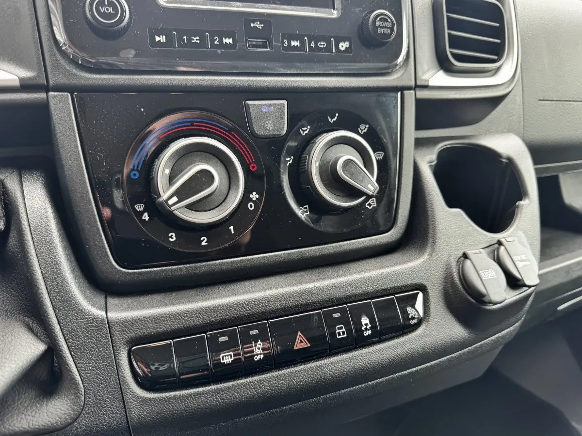 Gros plan sur la console centrale noire du Peugeot Boxer Fourgon blanc, avec commandes climatisation et ports USB visibles.