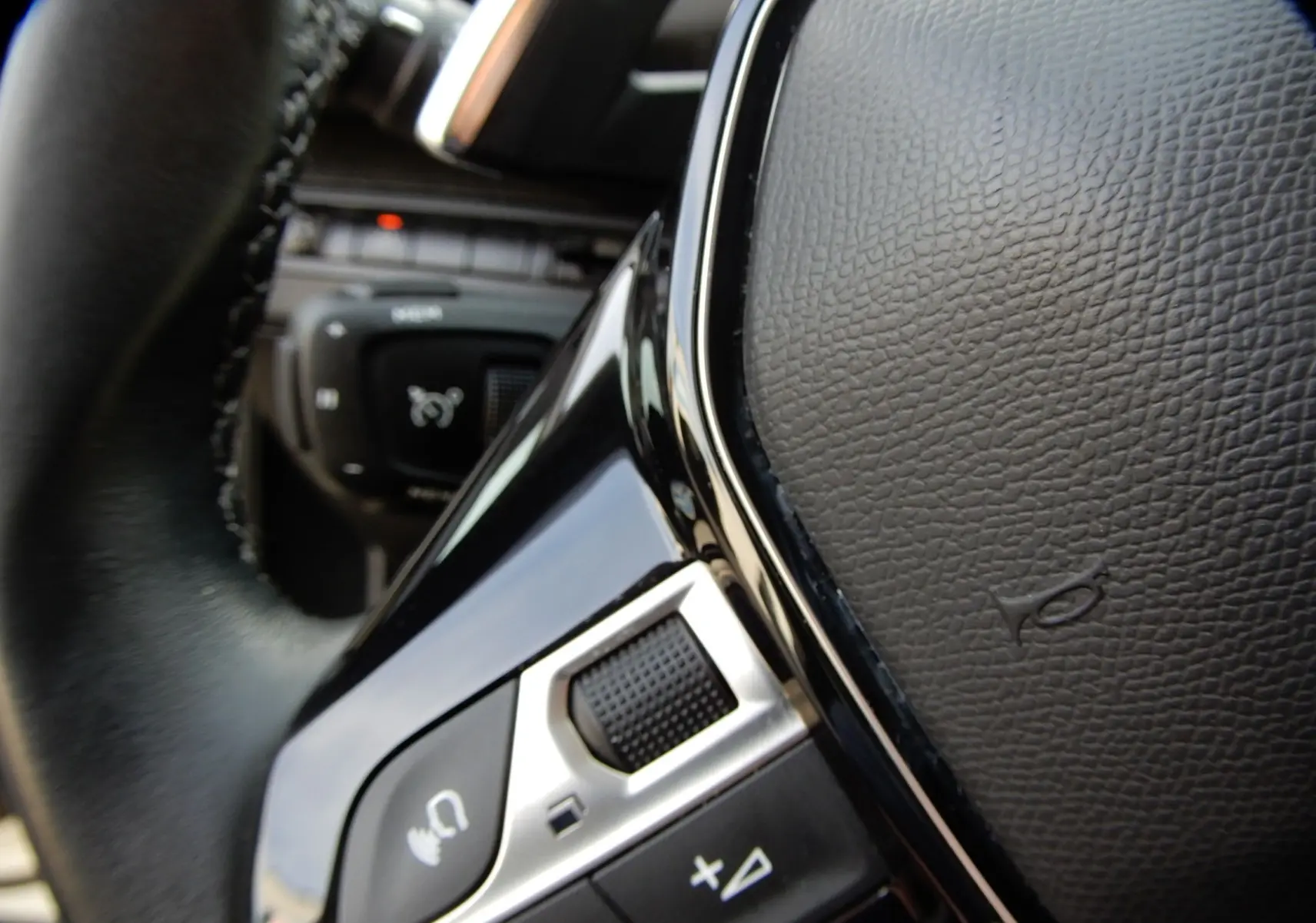 Gros plan sur la commande vocale et les boutons de volume du volant en cuir noir du Peugeot 5008 blanc nacré.