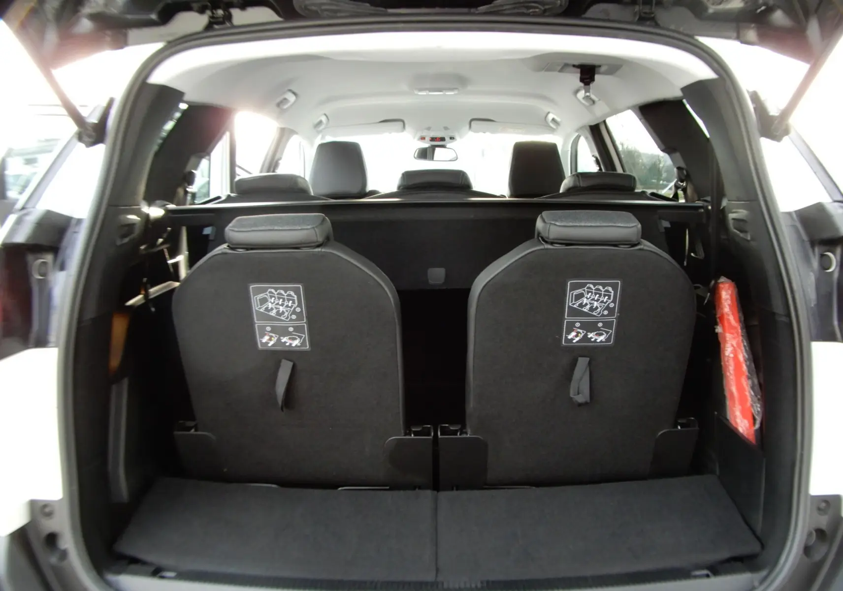 Vue arrière ouverte du coffre d'un Peugeot 5008 blanc nacré, montrant les dossiers des sièges rabattus et les appuie-têtes noirs.