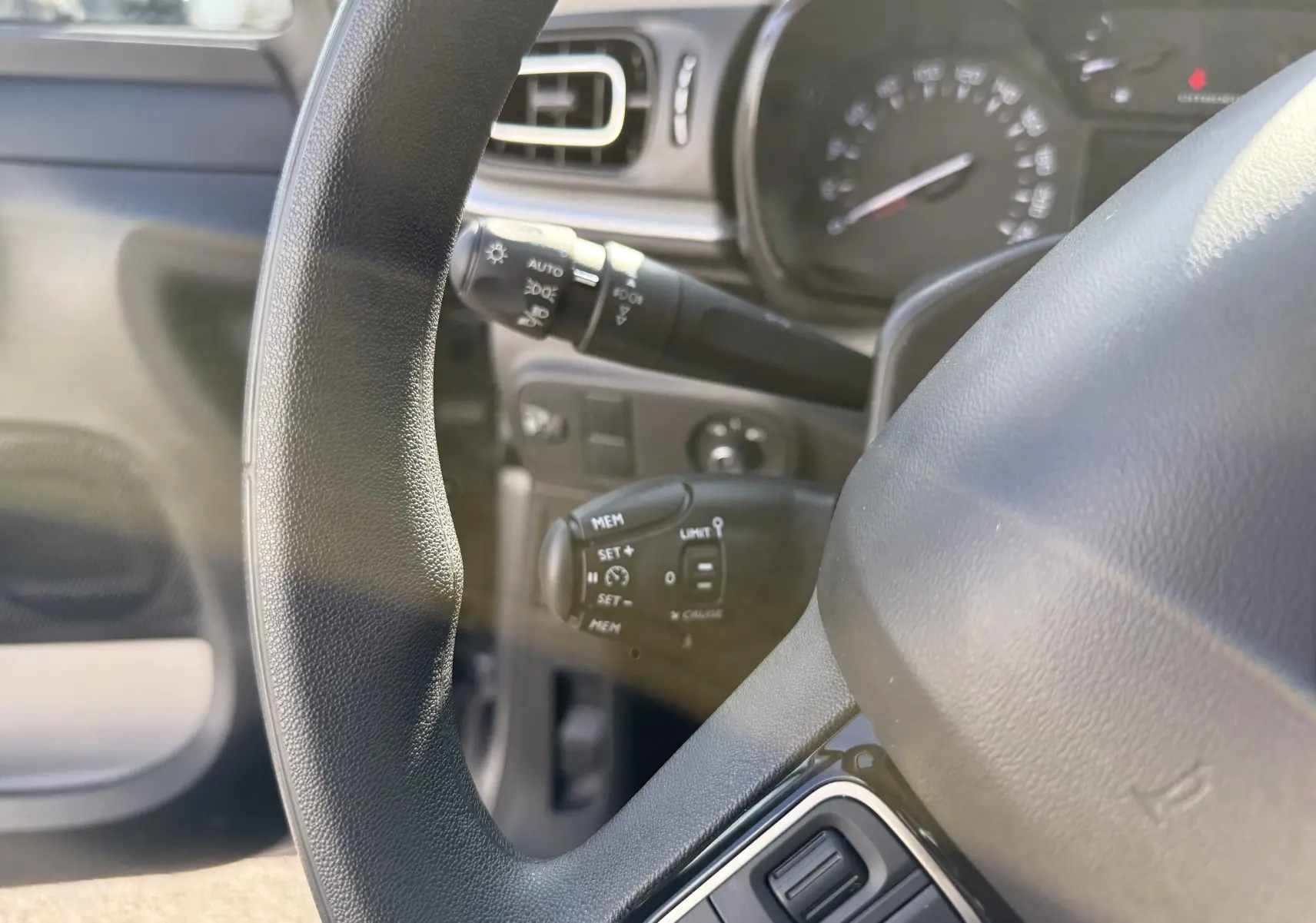 Gros plan sur le volant et le tableau de bord de la Citroën C3 gris acier, montrant les commandes au volant et les compteurs.