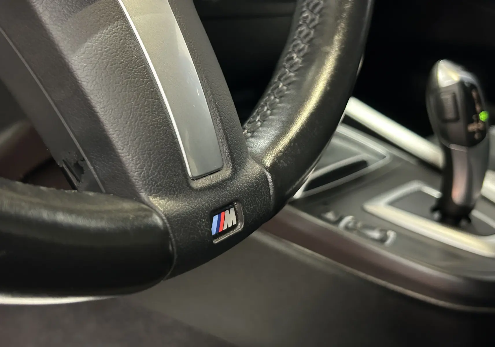 Gros plan sur le volant cuir noir avec logo M et levier de vitesse automatique de la BMW Série 1 120iA M Sport blanche.