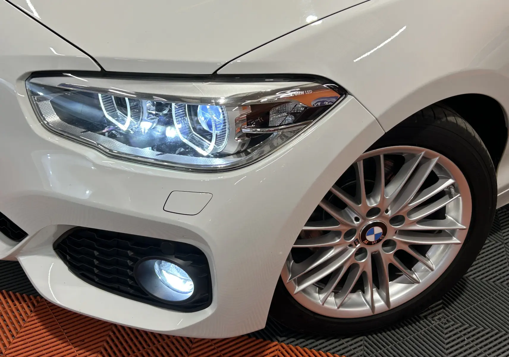 Gros plan sur l'avant droit blanc d'une BMW Série 1 120iA M Sport avec phares LED et jante alliage multibranches.