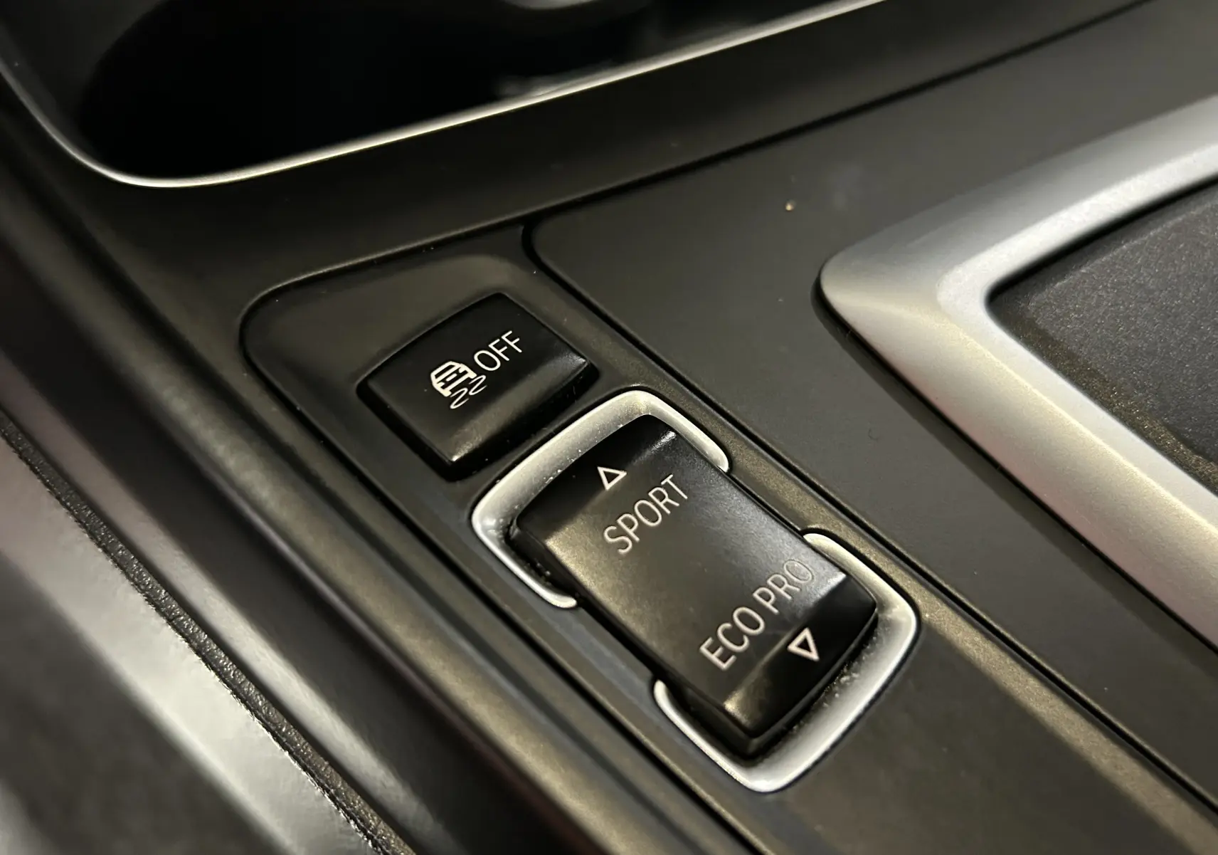 Gros plan sur les boutons de mode de conduite Sport et Eco Pro dans la console centrale d'une BMW Série 1 blanche.