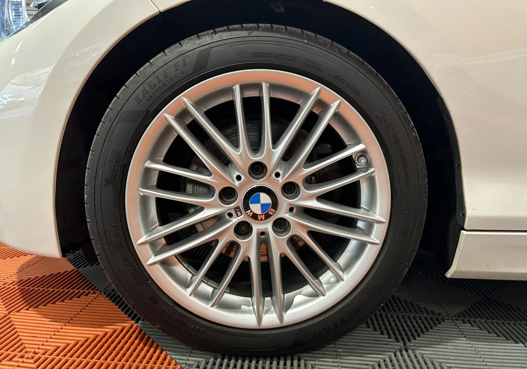 Gros plan sur la jante avant droite argentée d'une BMW Série 1 blanche, mettant en valeur le logo BMW central.