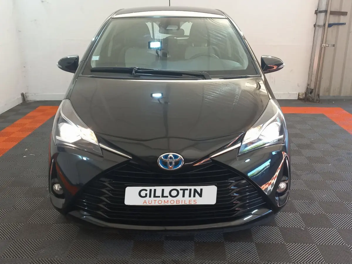 Vue frontale d'une Toyota Yaris noire 2018 avec phares allumés et calandre marquée en X dans un garage.