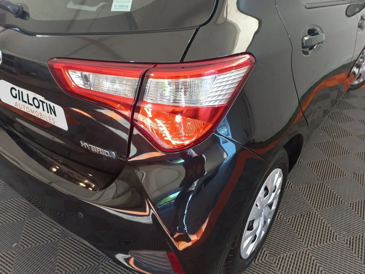 Vue 3/4 arrière droite d'une Toyota Yaris noire hybride, avec feu arrière distinctif et jante visible.