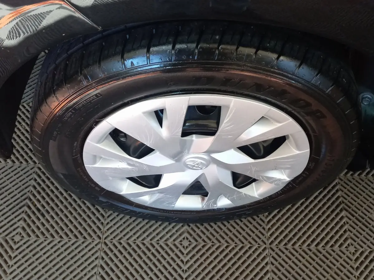 Gros plan sur la roue avant droite d'une Toyota Yaris noire, mettant en valeur la jante en plastique argenté et le pneu Dunlop.