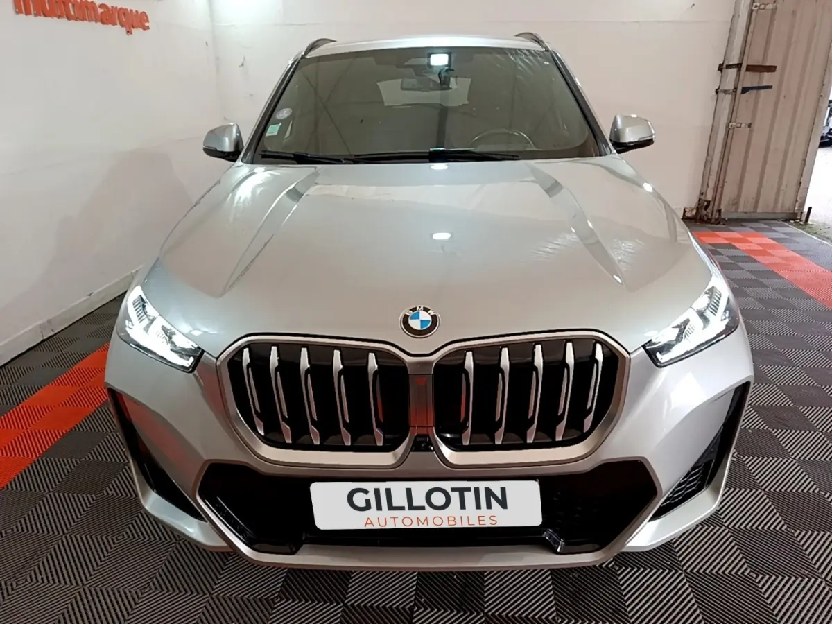 Vue avant d'une BMW X1 xDrive23i M Sport gris clair avec calandre imposante et phares LED allumés.