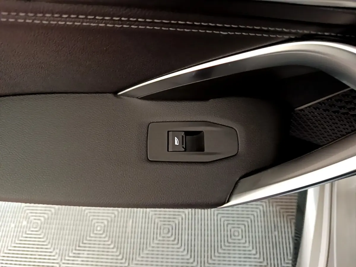 Gros plan sur la commande de vitre électrique intégrée dans la garniture noire de la porte côté conducteur du BMW X1 gris clair 2023.