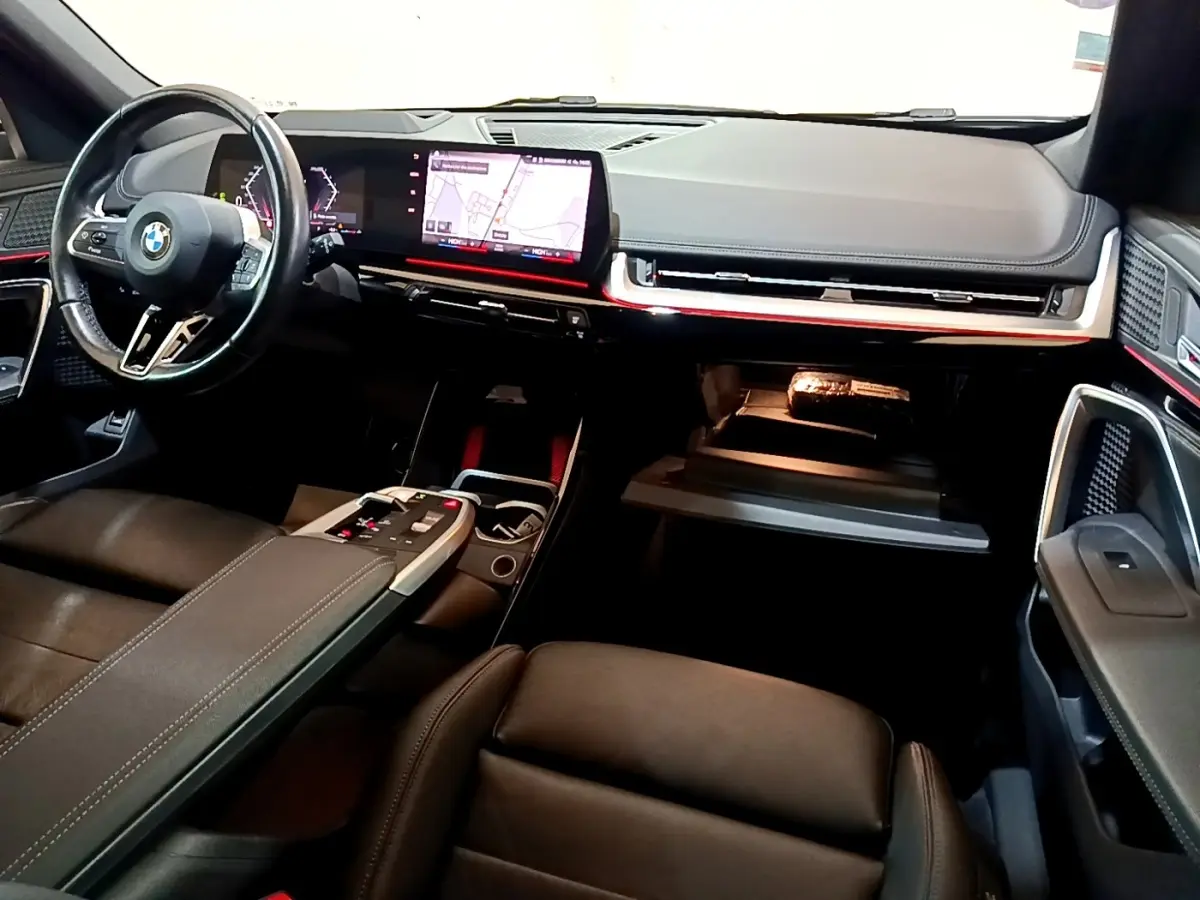 Vue intérieure avant droite du BMW X1 xDrive23i M Sport 2023, tableau de bord moderne avec écran tactile et éclairage d'ambiance rouge.
