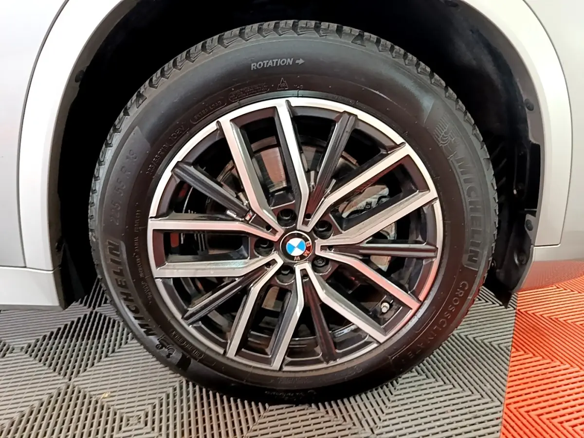 Gros plan sur la roue avant droite d’un BMW X1 gris clair, jante alliage M Sport à design étoilé.