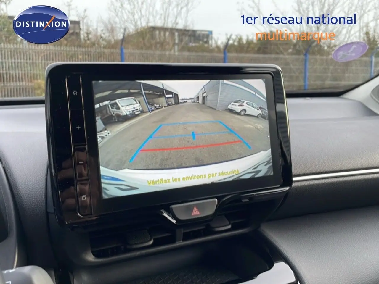 Écran central affichant la caméra de recul d'une Toyota Yaris Cross blanche, vue intérieure du tableau de bord.