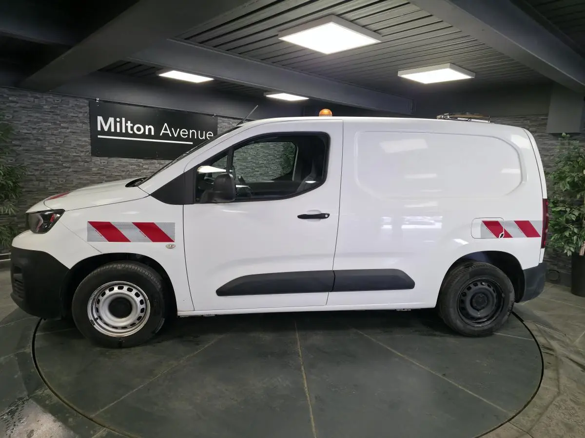 Vue de profil côté gauche d’un Peugeot Partner blanc avec bandes réfléchissantes rouges et blanches sur ailes avant et arrière.