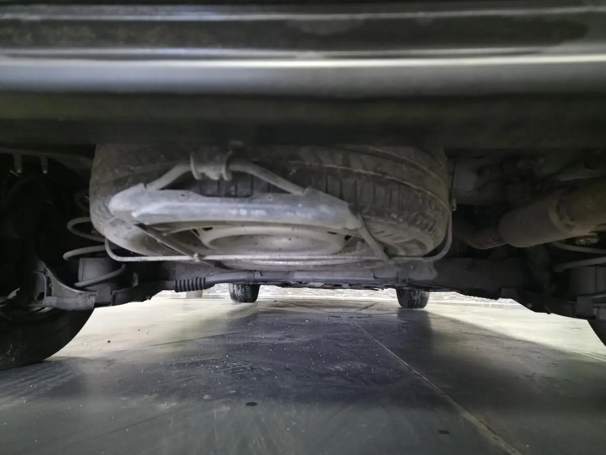 Vue en contre-plongée sous le Peugeot Partner blanc, montrant la roue de secours et le châssis arrière.