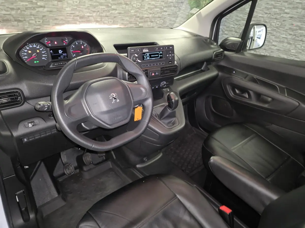 Intérieur du Peugeot Partner 2021 vu côté conducteur, tableau de bord noir avec volant et sièges en cuir noir.