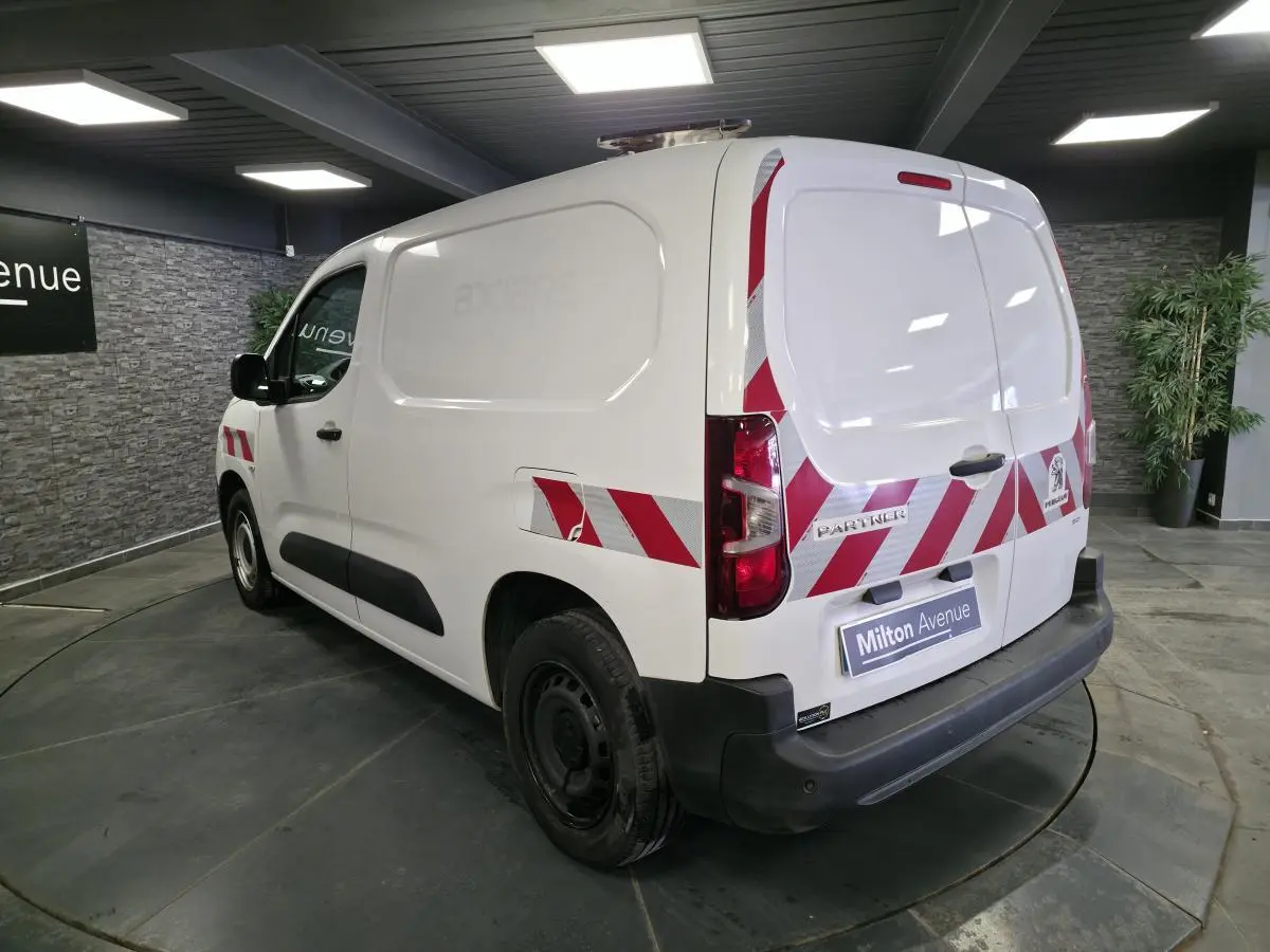 Vue 3/4 arrière droite d’un Peugeot Partner blanc avec bandes réfléchissantes rouges et blanches sur les portes arrière et latérales.